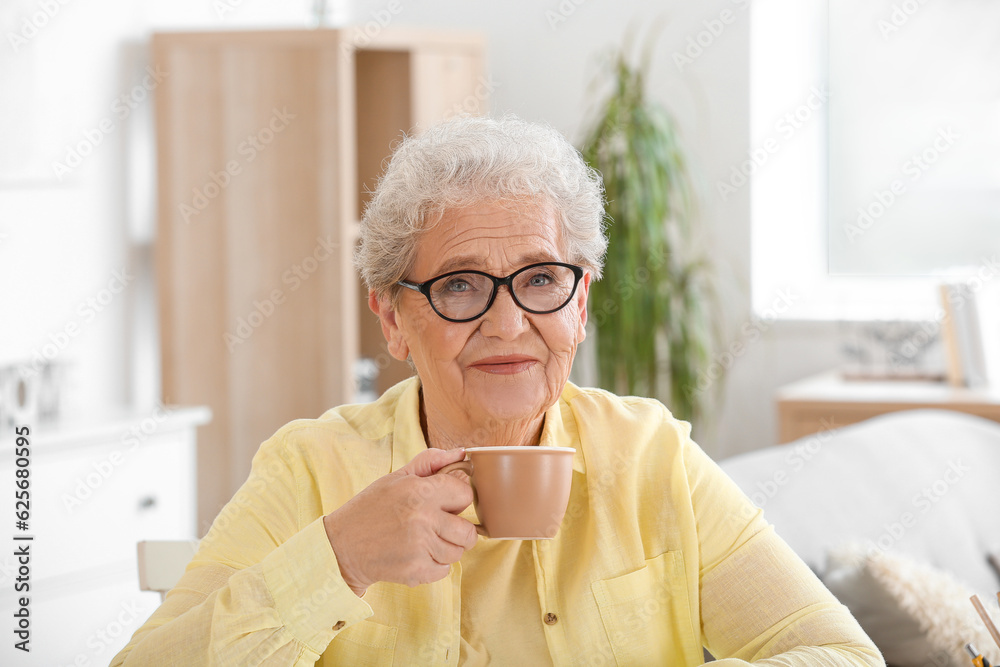 Senior woman in eyeglasses drinking tea at home