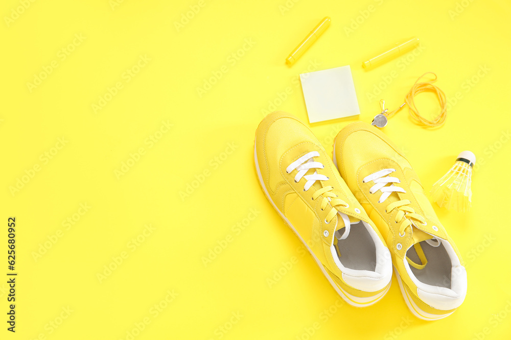 Sneakers with whistle, shuttlecock and stationery on yellow background