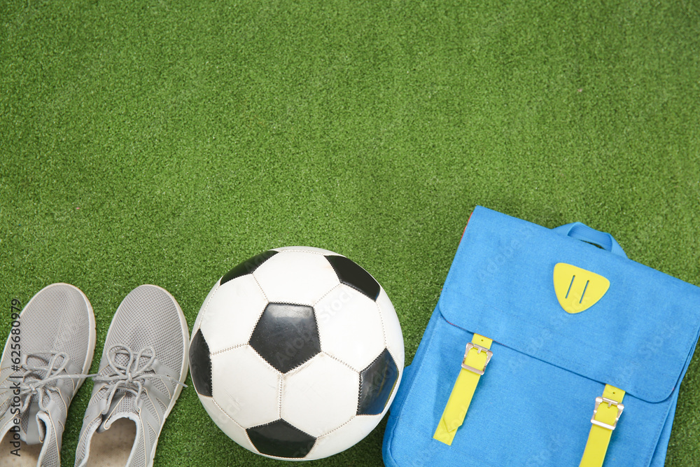 Sneakers with backpack and soccer ball on color background