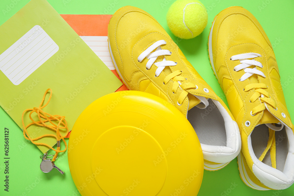 Sneakers with frisbee, tennis ball, whistle and notebooks on green background