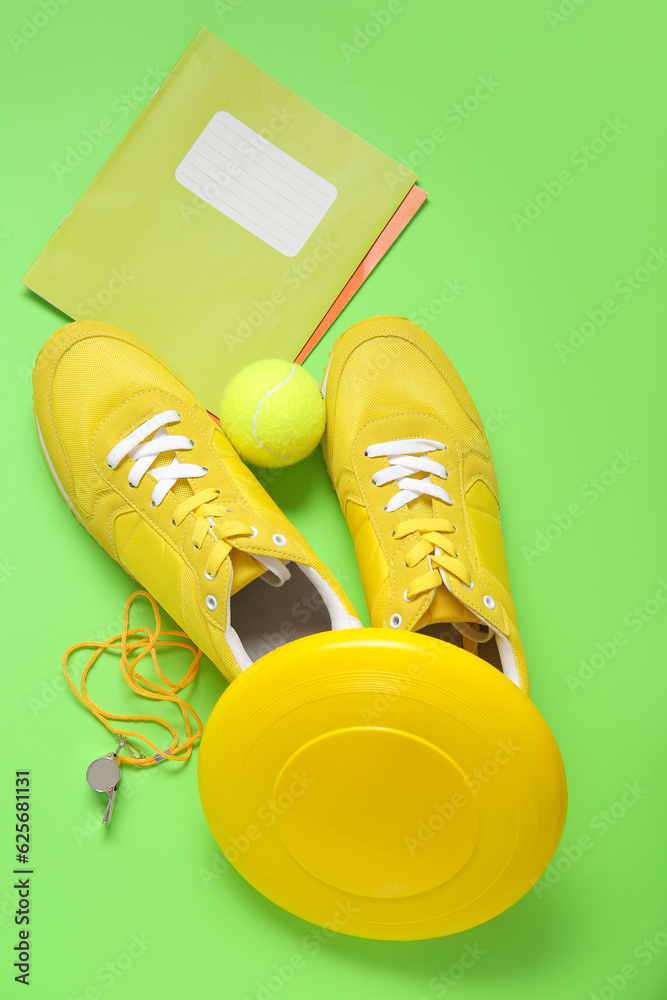 Sneakers with frisbee, tennis ball, whistle and notebooks on green background