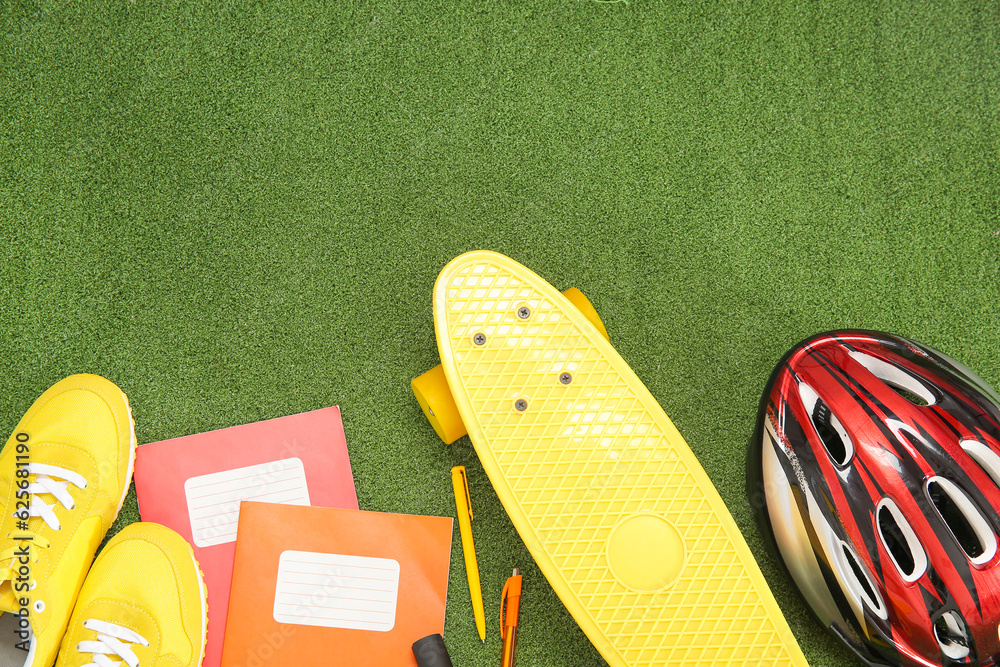 Bike helmet with sneakers, skateboard and different stationery on color background