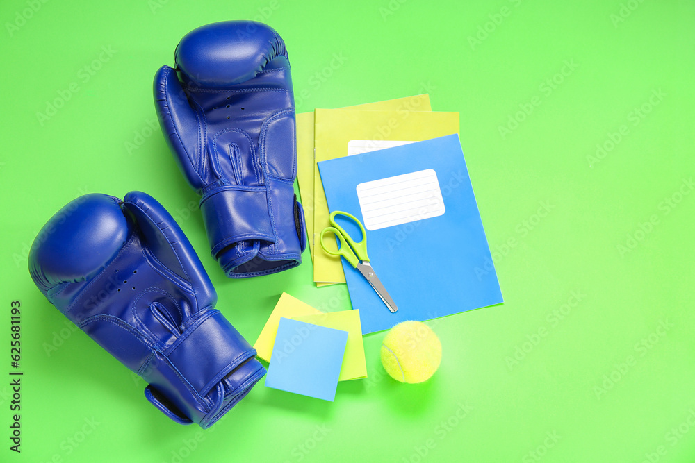 Boxing gloves with tennis ball and different stationery on green background