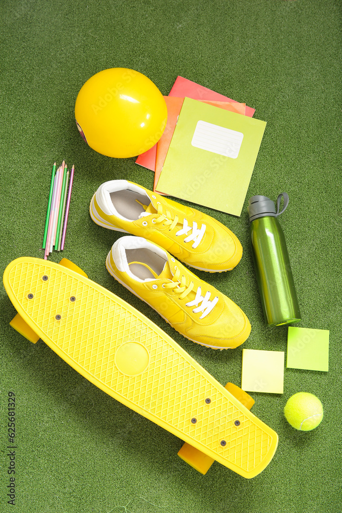 Sneakers with bottle of water, sport equipment and different stationery on color background