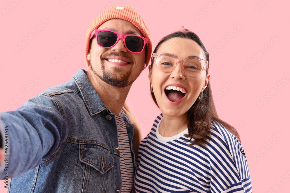 Happy young couple taking selfie on pink background, closeup