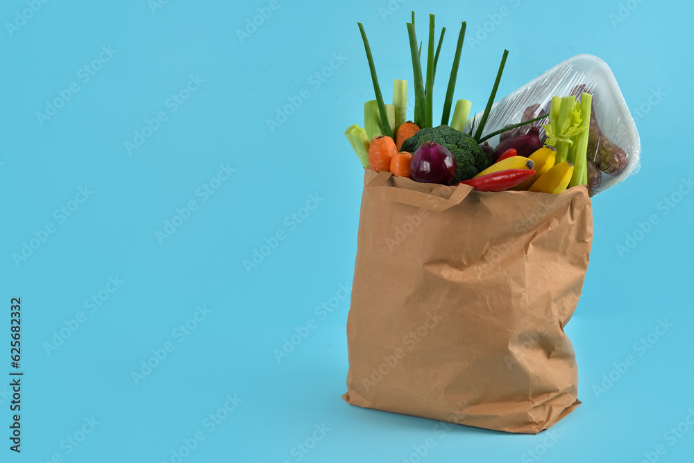 Paper bag full of fresh vegetables and sausages on blue background