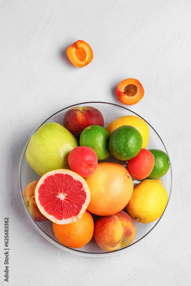 Bowl with different fresh fruits on grey background