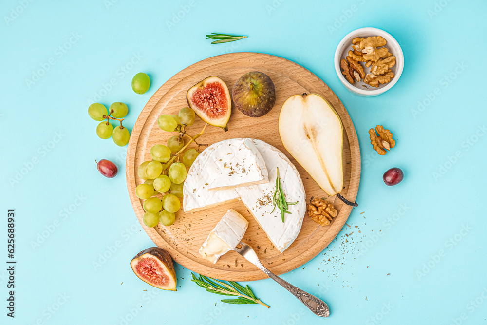 Wooden board with pieces of tasty Camembert cheese, nuts and fruits on blue background