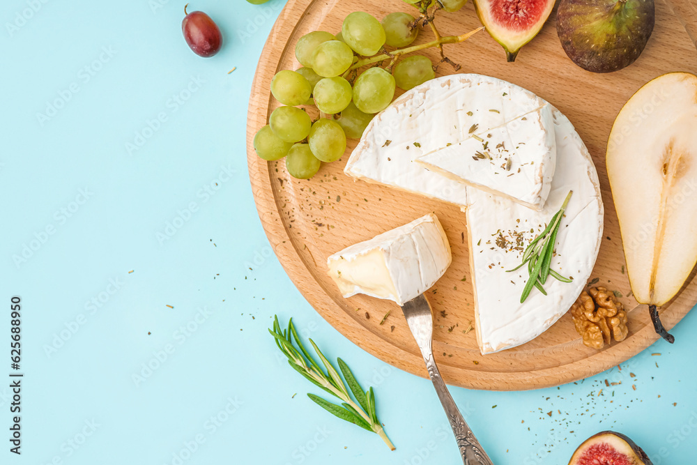 Wooden board with pieces of tasty Camembert cheese on blue background