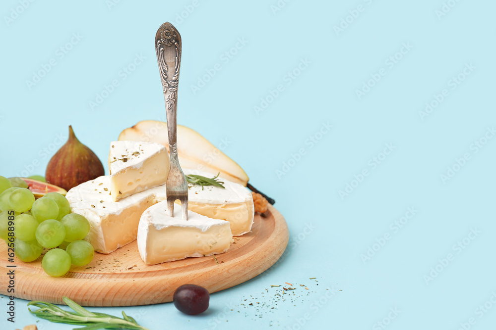 Wooden board with pieces of tasty Camembert cheese on blue background