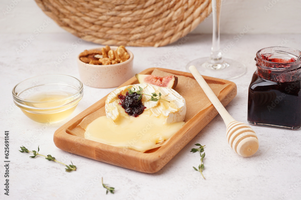 Wooden board of tasty baked Camembert cheese on light background