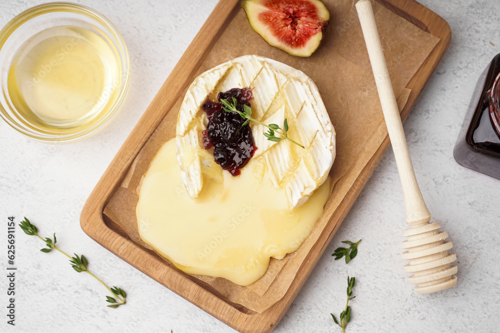 Wooden board of tasty baked Camembert cheese on light background