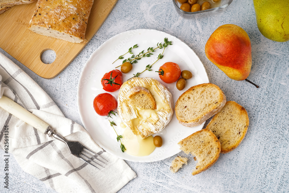 Plate of tasty baked Camembert cheese on light background