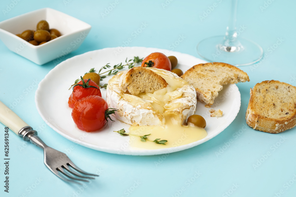 Plate of tasty baked Camembert cheese on blue background