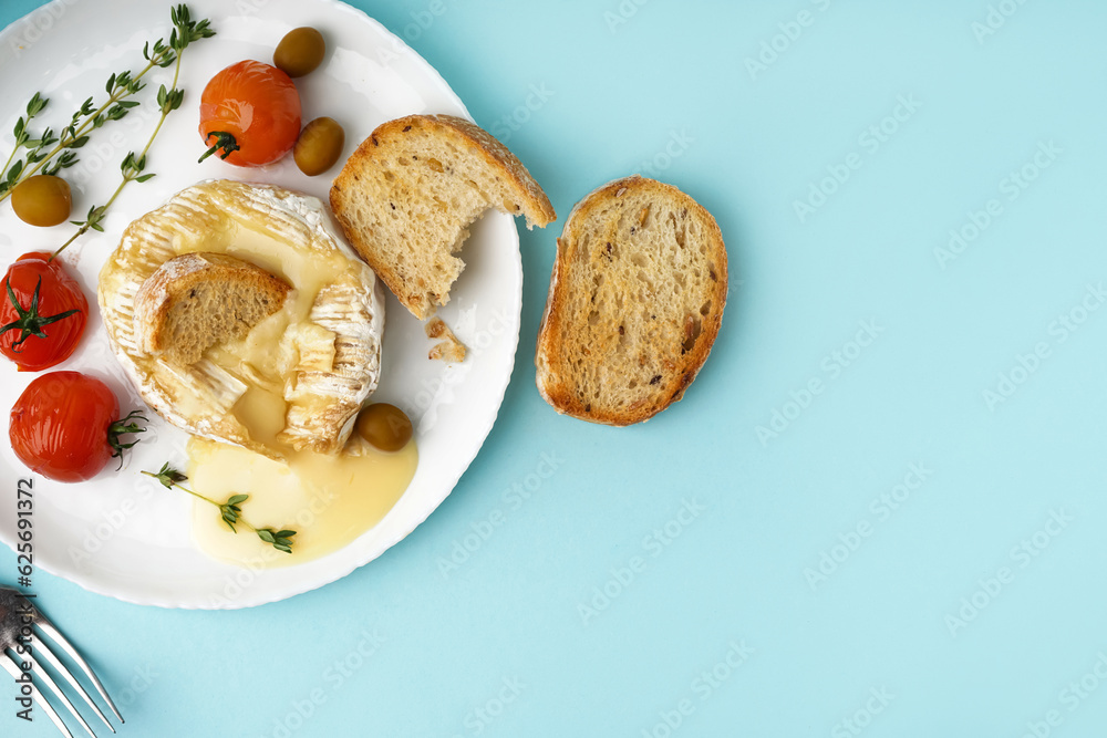 Plate of tasty baked Camembert cheese on blue background