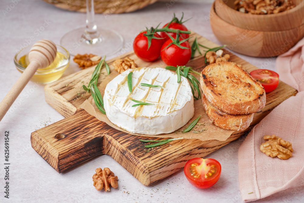 Wooden board with tasty baked Camembert cheese on light background