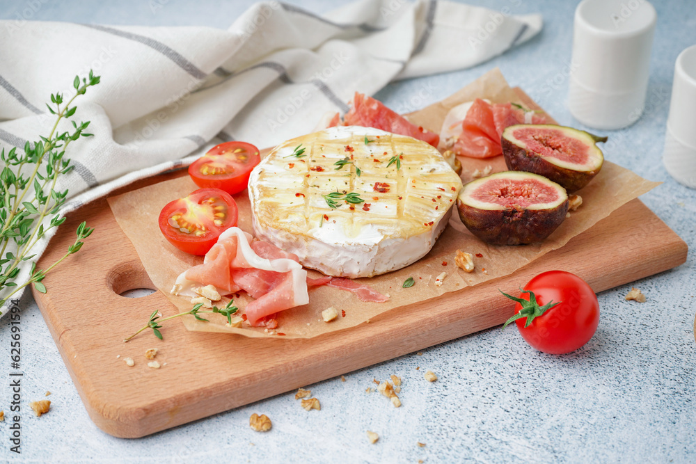 Wooden board with tasty baked Camembert cheese on light background