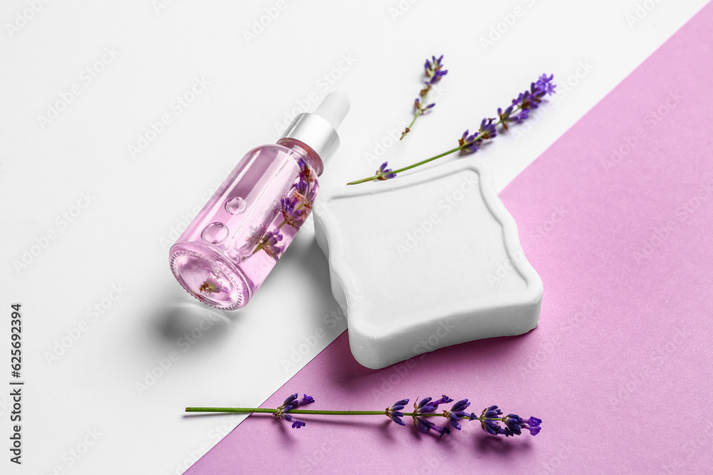 Bottle of essential oil, soap bar and lavender flowers on color background