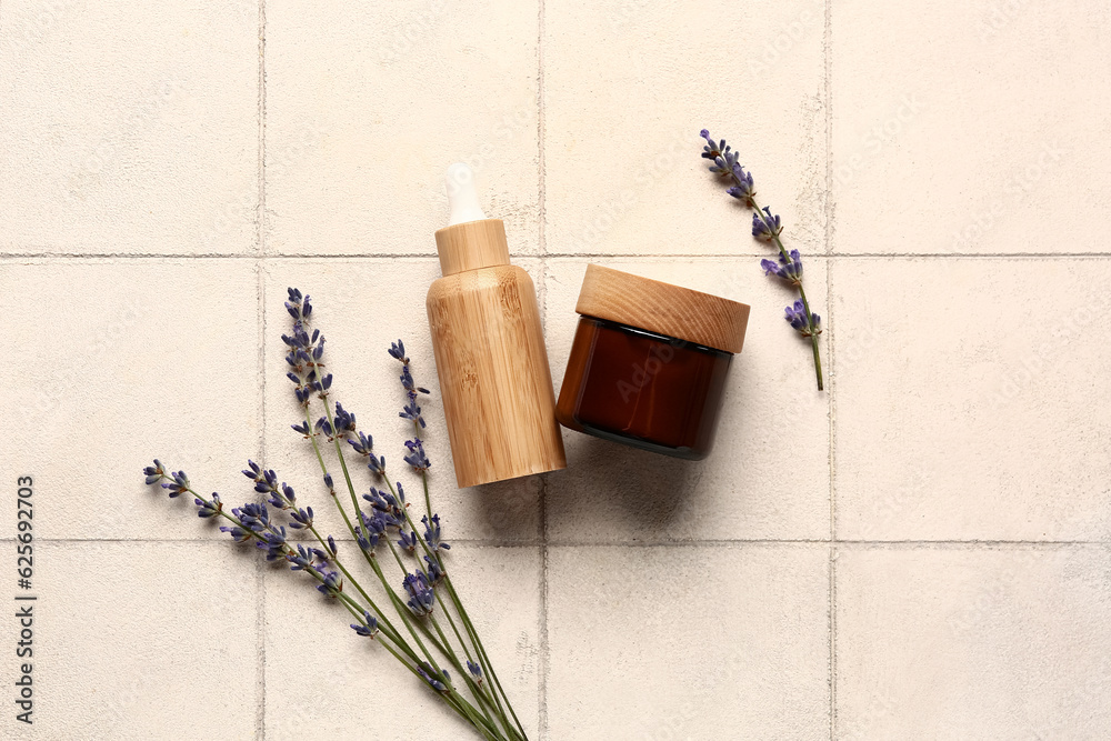 Cosmetic products and lavender flowers on light tile background