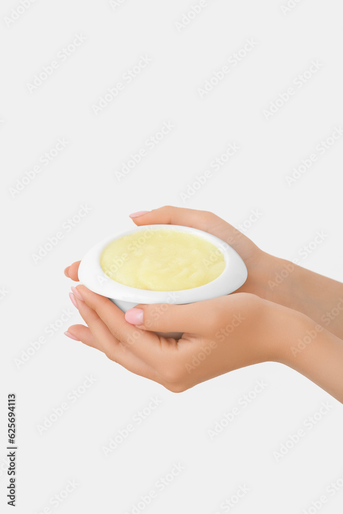 Female hands with bowl of lemon body scrub on white background