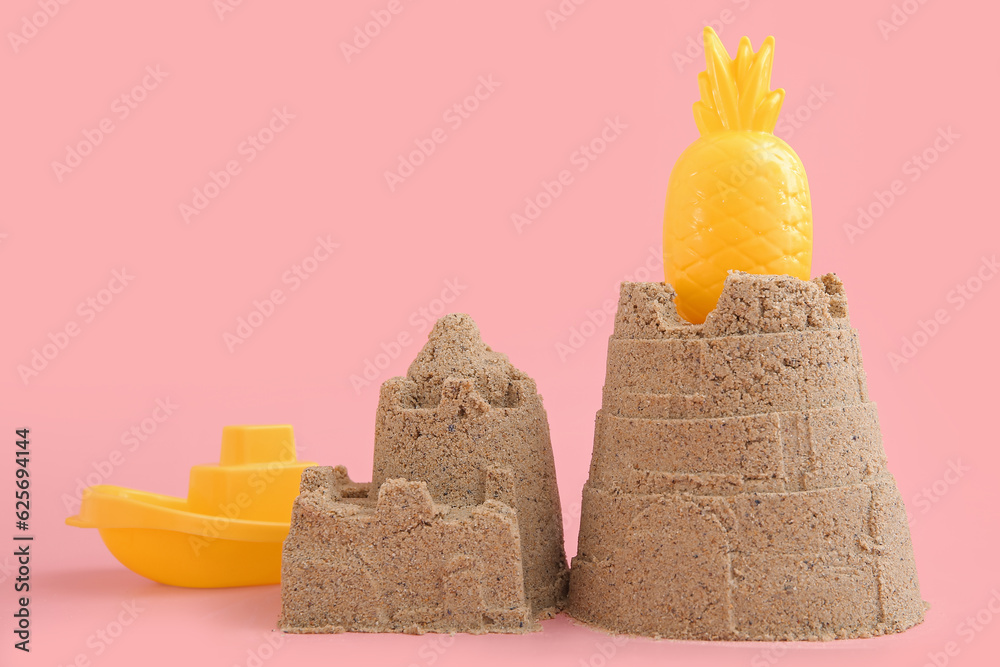 Castle made of sand with beach toys for children on pink background