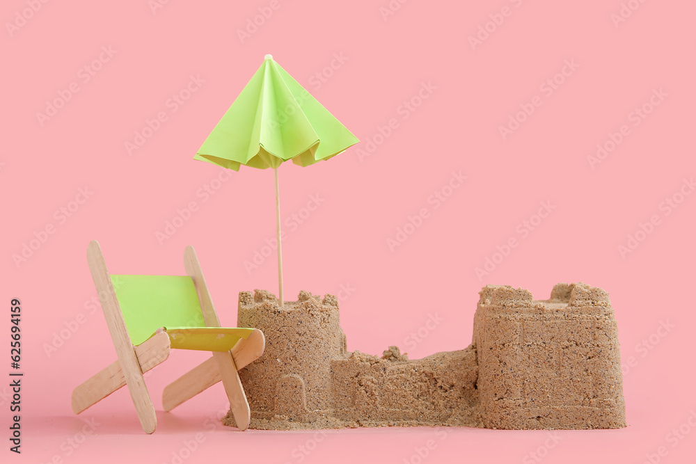 Castle made of sand with mini deckchair and umbrella on pink background