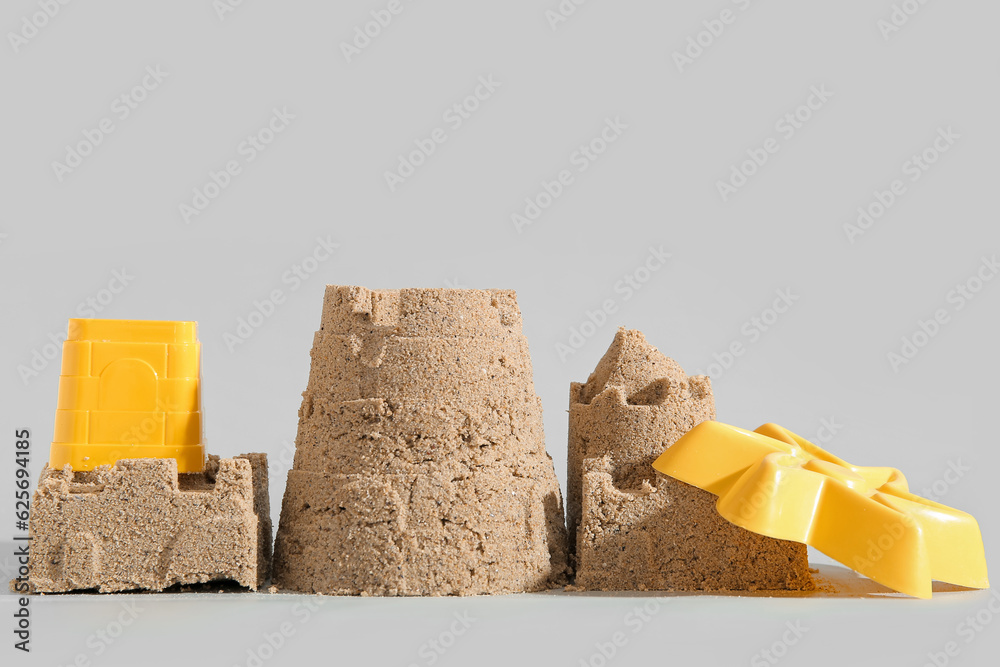 Castle made of sand with beach toys on grey background