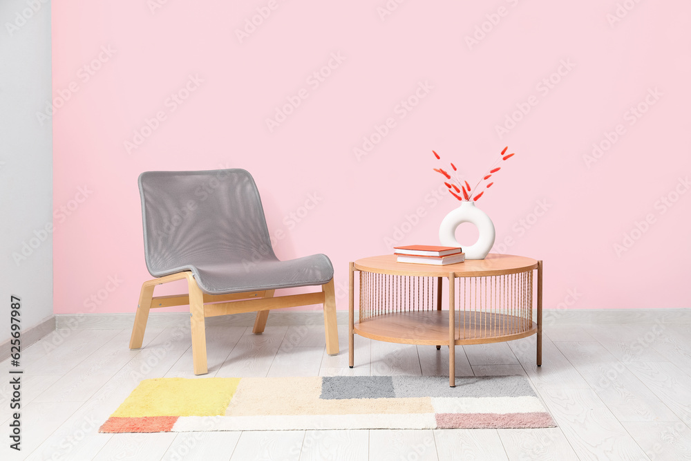 Grey armchair, coffee table and stylish rug near pink wall