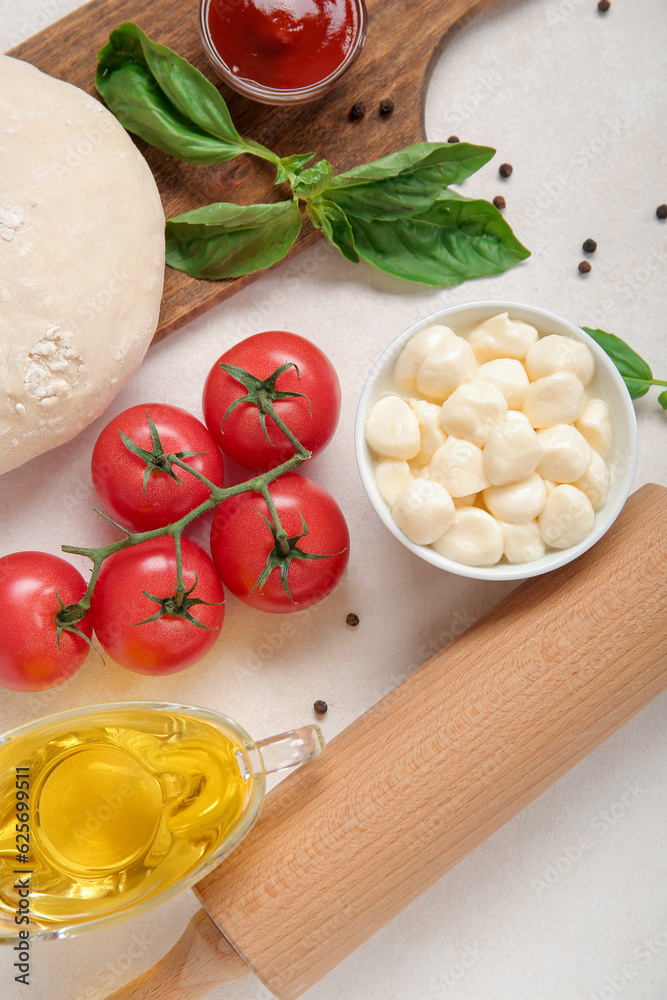 Raw dough and ingredients for preparing pizza on light background