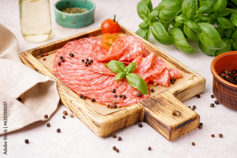 Wooden board with slices of tasty salami on light background