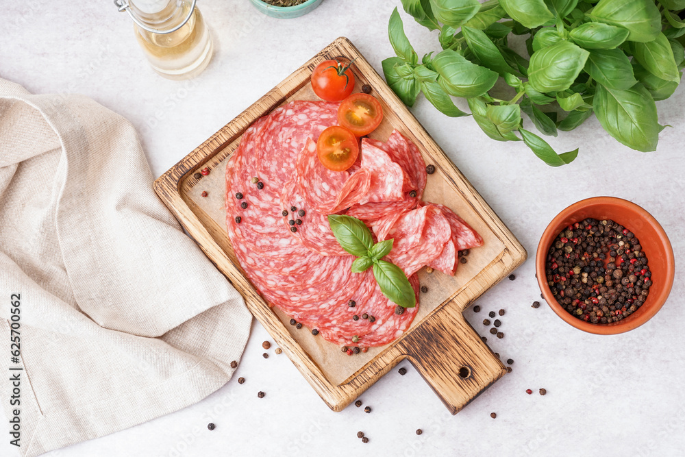 Wooden board with slices of tasty salami on light background