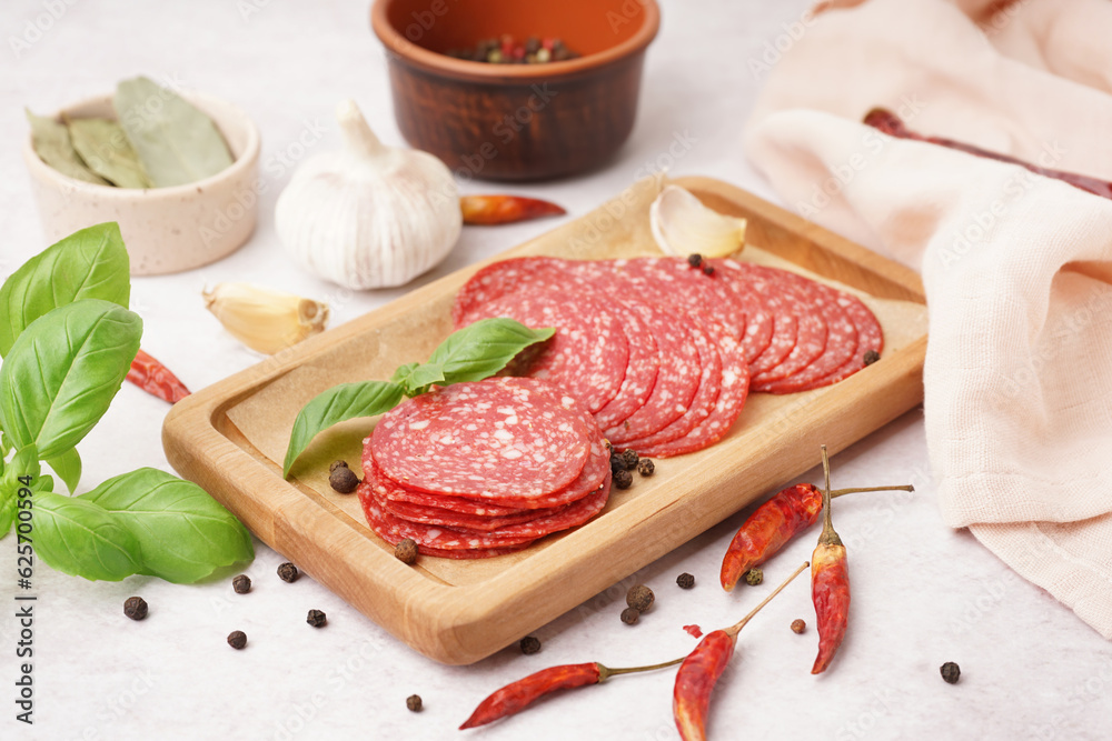 Wooden board with slices of tasty salami on light background