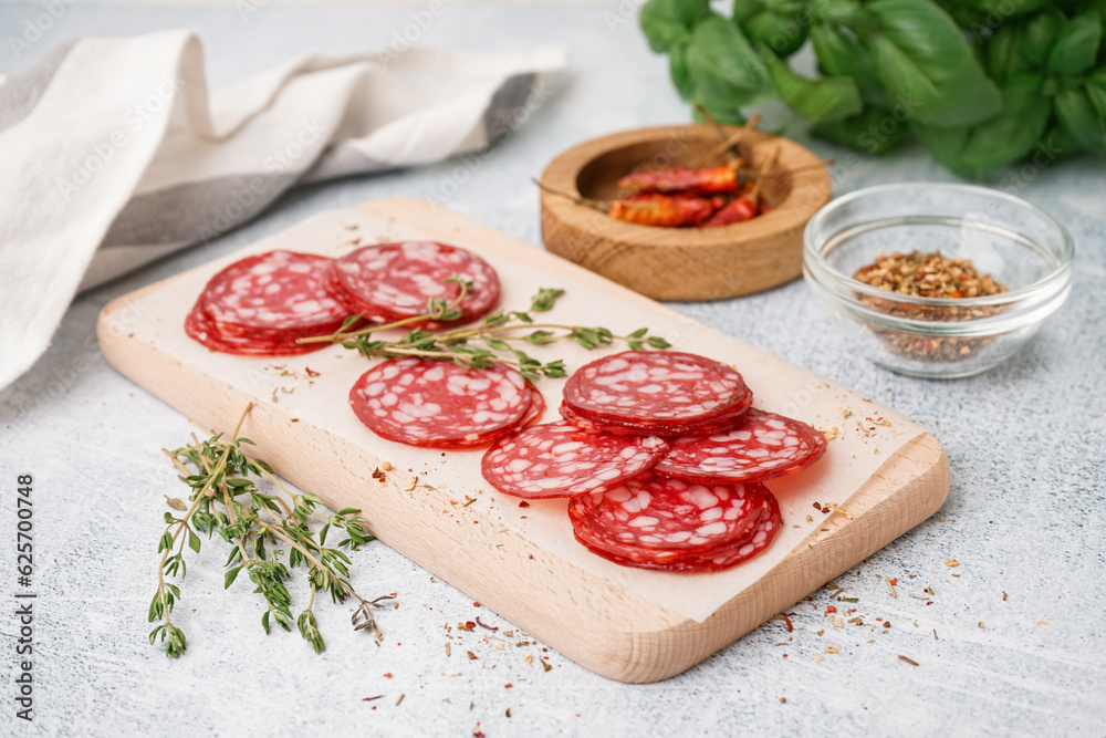 Wooden board with slices of tasty salami on light background