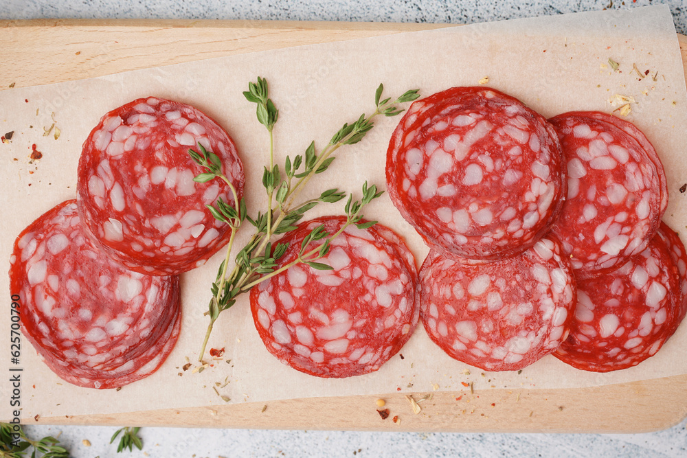 Wooden board with slices of tasty salami on light background