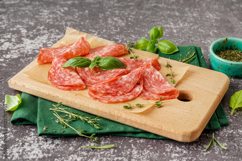 Wooden board with slices of tasty salami on grey background