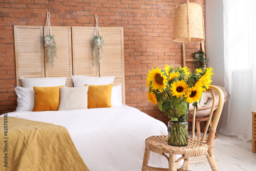 Vase with beautiful sunflowers on wicker chair in interior of stylish bedroom