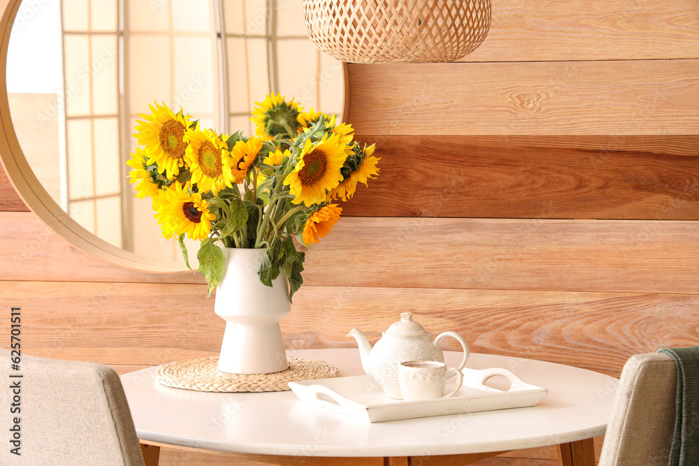 Vase with beautiful sunflowers on dining table with teapot