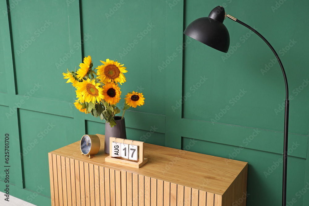 Vase with beautiful sunflowers on wooden cabinet near green wall