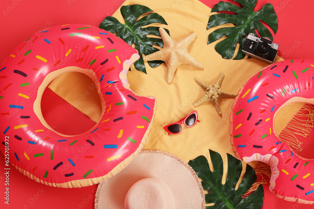 Inflatable rings in shape of donuts with beach accessories on red background