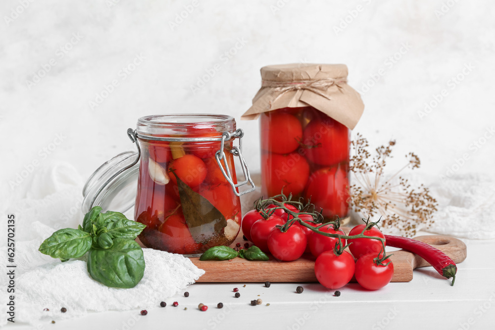 Jars with canned tomatoes and basil on white wooden table