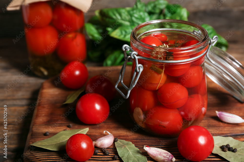 Jars with canned tomatoes and basil on wooden background