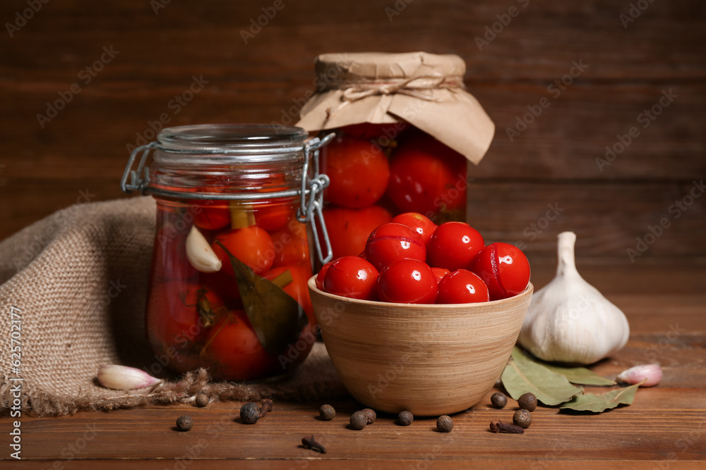 Jars and bowl with canned tomatoes on wooden background