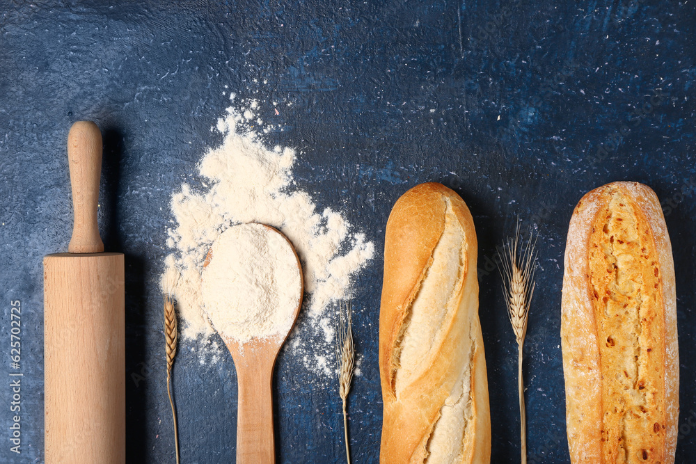 Composition with baguettes, flour, rolling pin and wheat ears on dark blue table