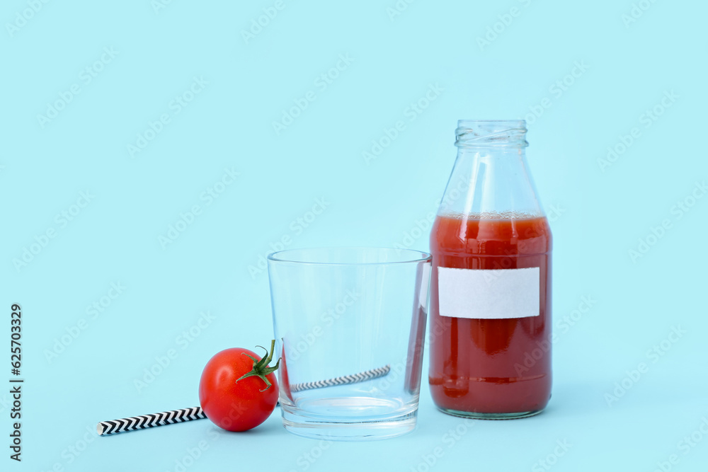 Empty glass and bottle of tasty tomato juice on blue background