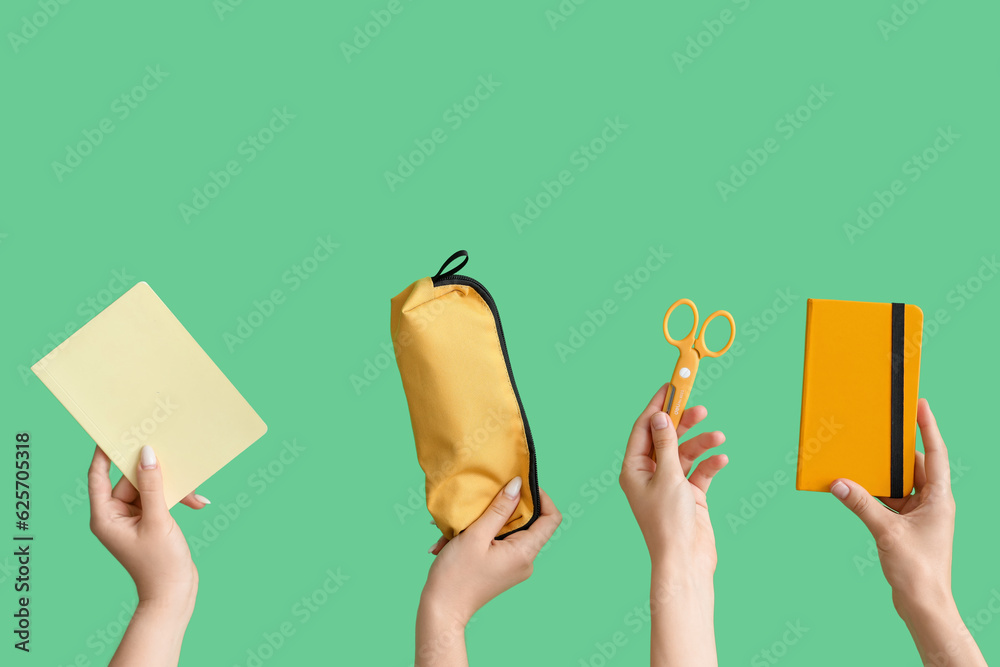 Female hands with school accessories on green background