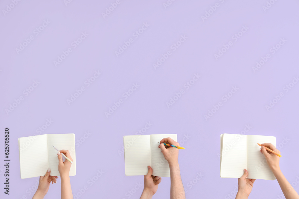 Hands writing in open notebooks on lilac background