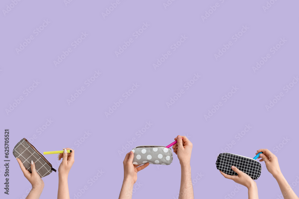 Hands with pencil cases on lilac background