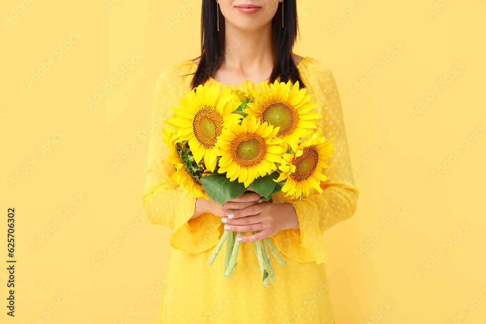 Young woman with beautiful sunflowers on yellow background