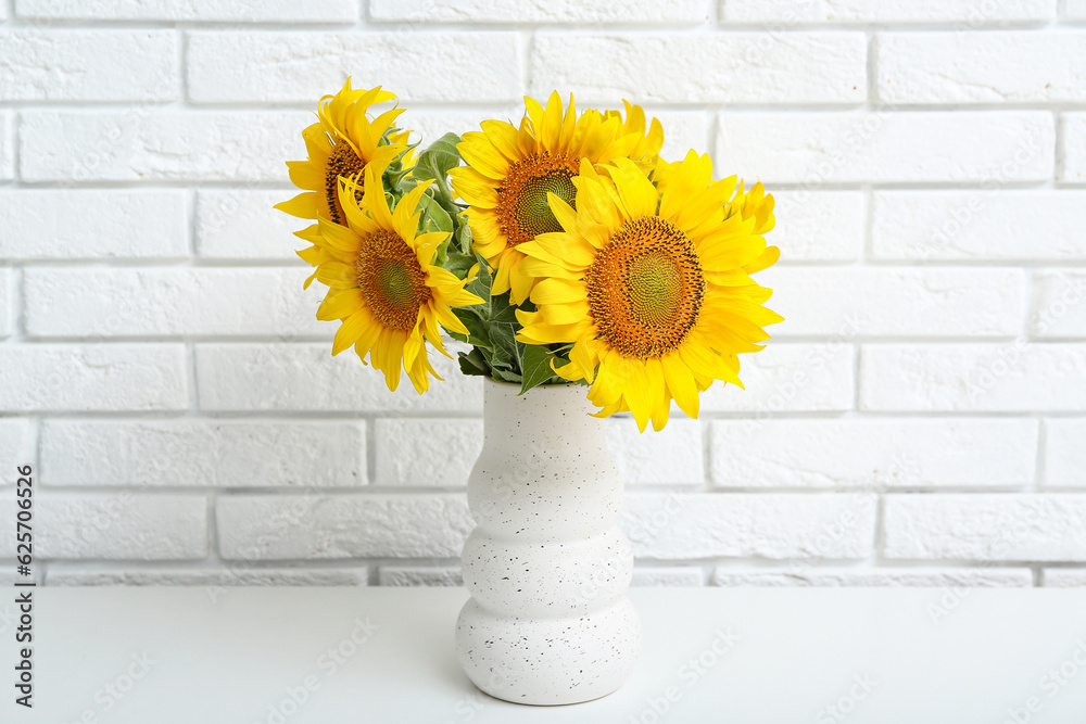 Vase with sunflowers on table near white brick wall