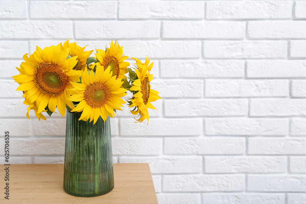 Vase with sunflowers on table near white brick wall